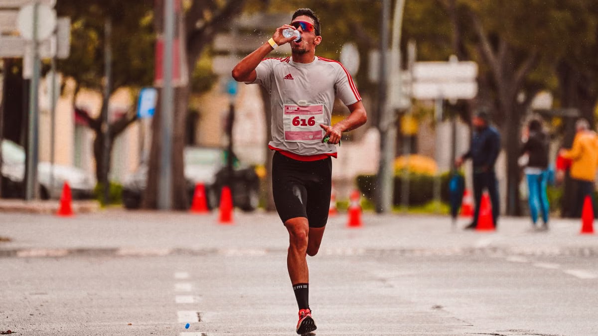 A dedicated runner drinks from a water bottle during a marathon on a city street.